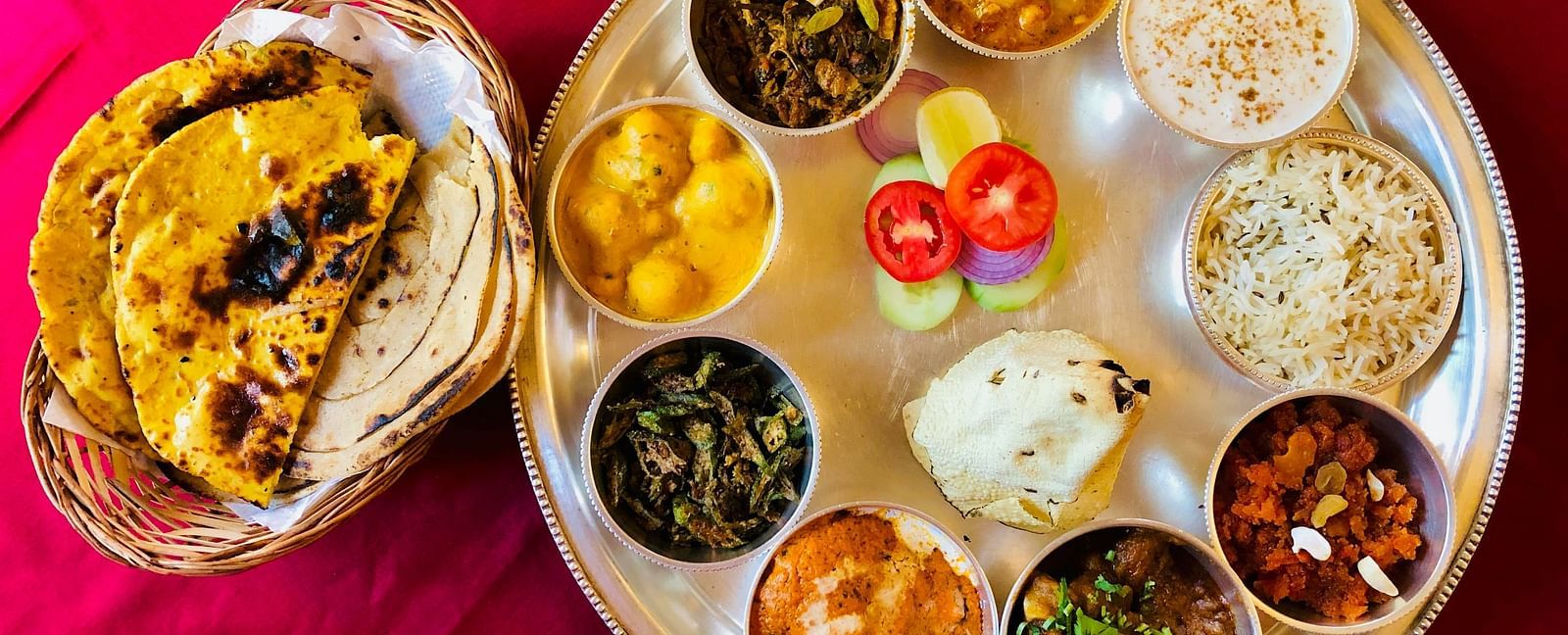 An aerial view of a Rajasthani Thali with many items on the plate next to a bowl of rotis.