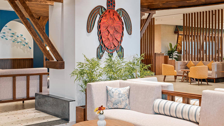 A diagonal view of the lounge features a spacious sofa, wooden table with flowers, sea-themed wall décor, and plants at Cloud9 Sarovar Premiere, Palolem Goa