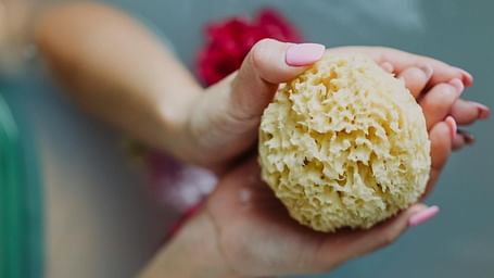 Hands gently holding a natural, textured loofah sponge.
