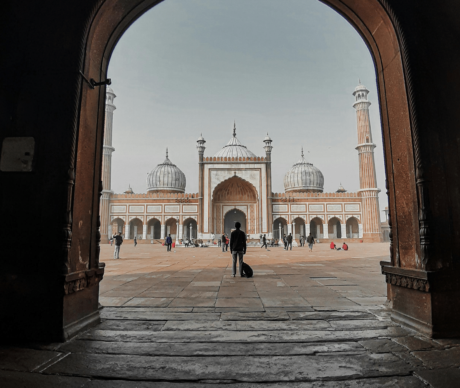 Historic monument seen through a large archway, with people walking toward it.