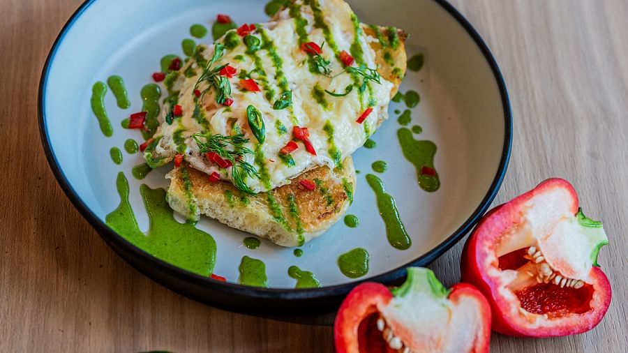 A plate of egg toast topped with sauces and veggies, with capsicum cut into two pieces and placed beside the plate, along with a chilli at Indie Stays Mumbai International Airport.