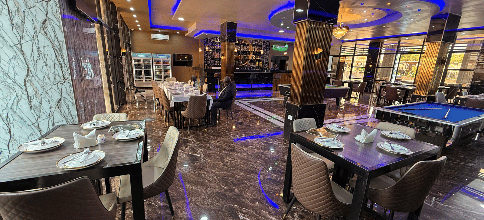 A lavish indoor dining area with marble-effect flooring, dark tables, place settings, and striking blue neon lighting at Luffu Club.