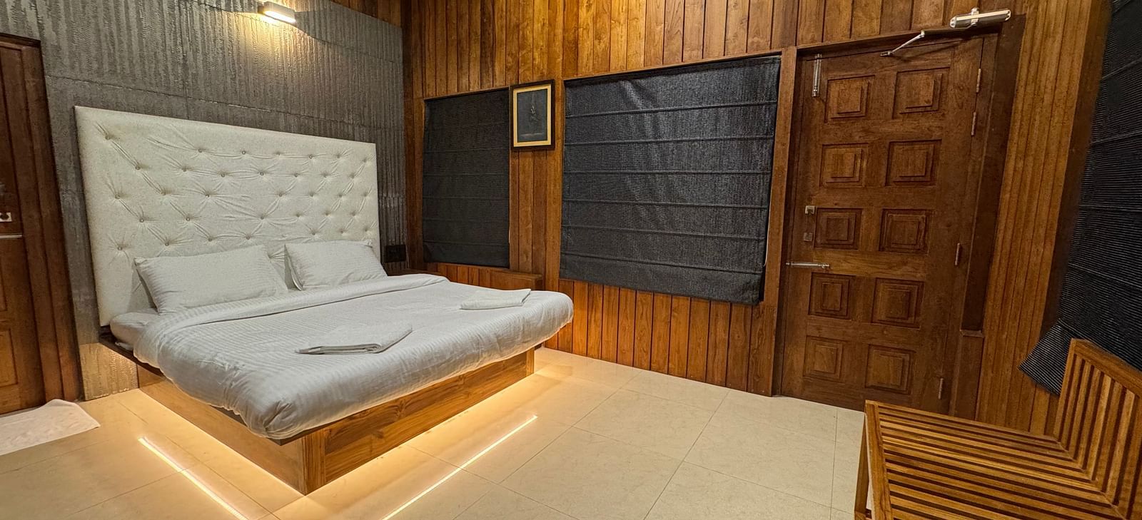 A bedroom with a modern platform bed with illuminated base, a white tufted headboard, and wooden paneling on the walls.