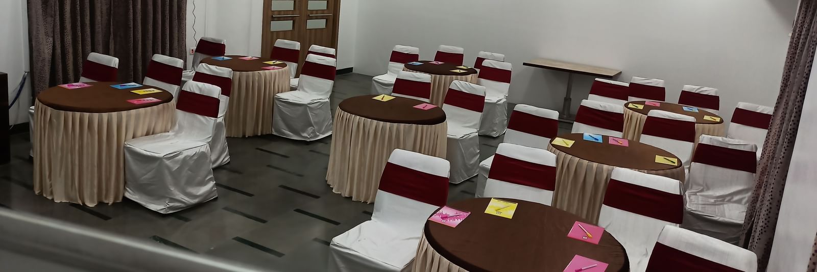 Cluster seating arrangement with white chairs tied in maroon sashes, set in a well-lit hall with neutral decor.