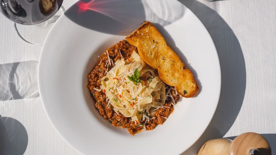 image of spaghetti prepared in red sauce garnished with cheese and served with a slice of garlic bread on side