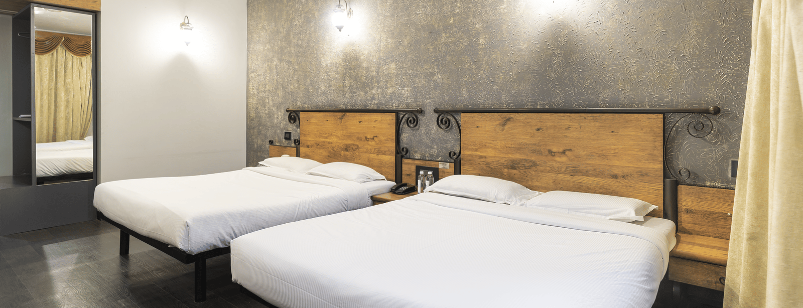 Bedroom with two double beds, wooden headboards and mirror at Infiniti Hotel, Indore.