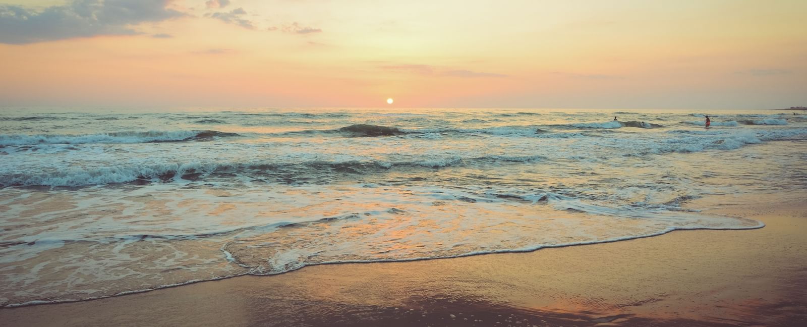 Waves overlapping on the beach with the setting sun in the background.