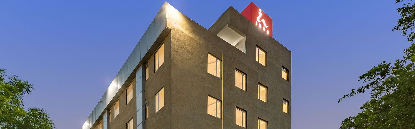 A facade image of a well-lit Inde Cyber City, Gurgaon building and beyond it an evening sky can be seen in the background - Inde Hotels & Resorts