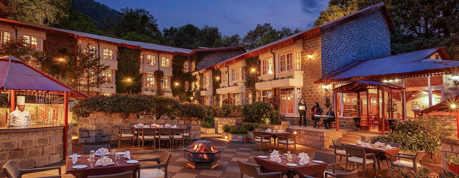 Outdoor restaurant seating beneath a dark sunset sky and surrounded by trees.