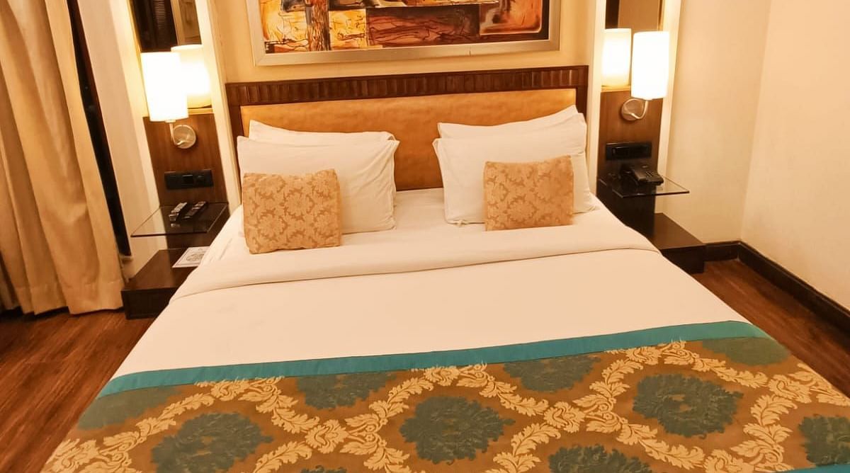 Suite with a double bed neatly arranged with plush pillows, bedside tables each topped with a lamp, and a photo frame on the headboard at Inde Signature Tower, Gurgaon