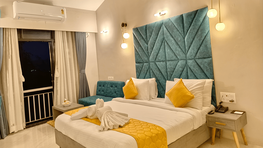 A side view double bed room with head board, side table, balcony with curtains, rug and AC
