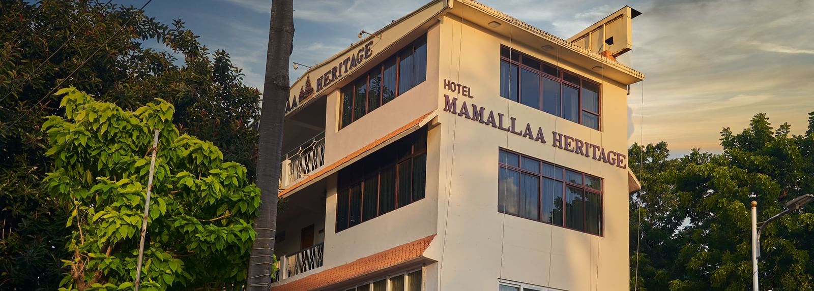 The exterior of Hotel Mamallaa Heritage from a slightly different angle, showcasing its multi-story structure and architectural details under a pleasant sky.
