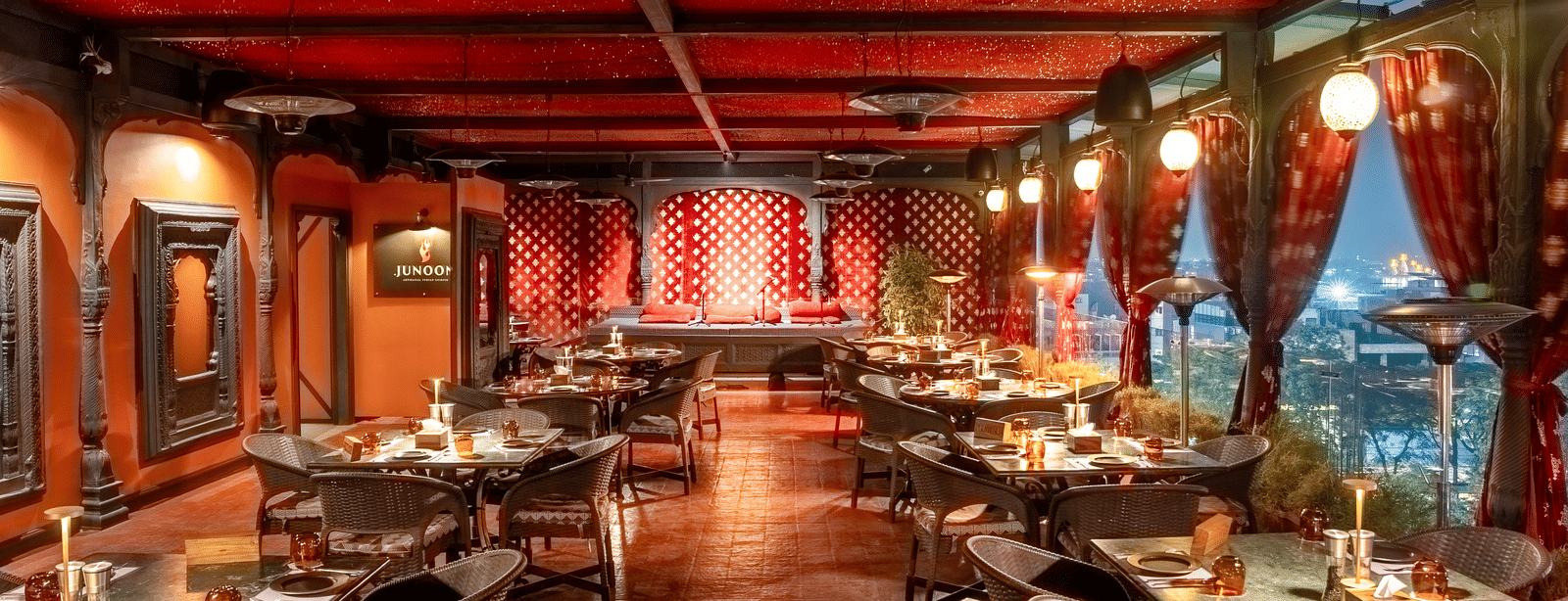 A large restaurant hall with red ceiling, long rows of dining tables and warm hanging lights at Infiniti Hotel, Indore.
