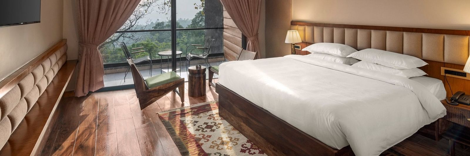 A cosy bedroom with a wooden floor and ceiling, large draped window with a scenic view, and a comfortable sitting area - The Samai, Bhimtal