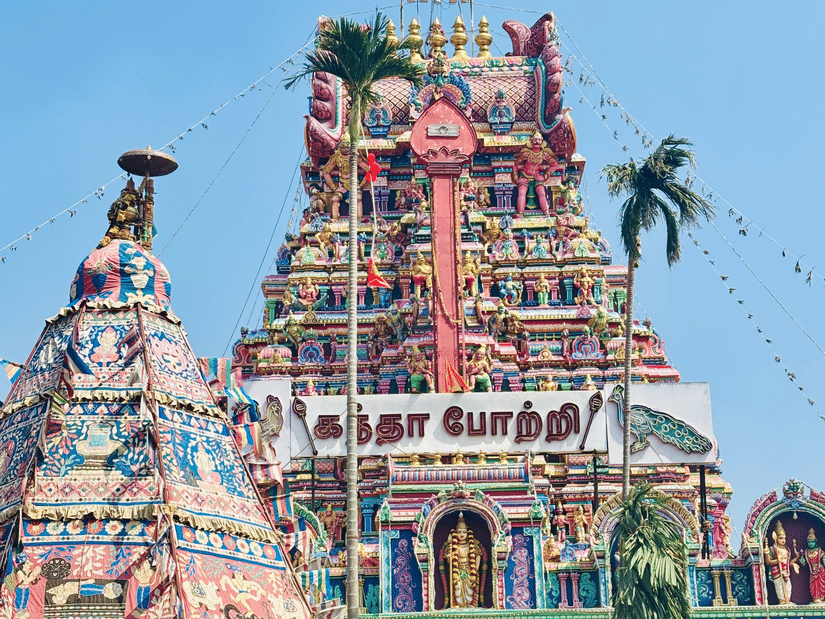 Front view of an ornate, colorful South Indian temple structure decorated with festive banners under a clear blue sky.