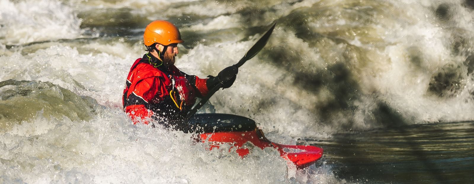 A person paddling in a bright red raft on a rushing river, doing an adventurous rafting experience.