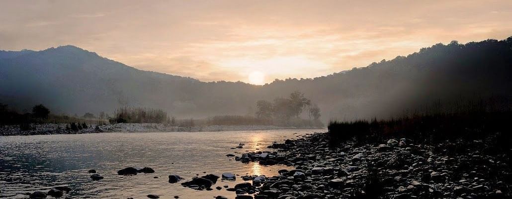 A photo with a beautiful sunset over a river and mountains in the background.