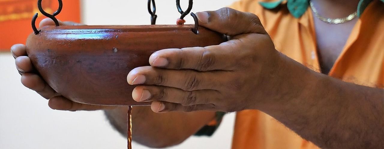 a person holding a clay pot with a small hole in the bottom to let the oil flow down through a thread