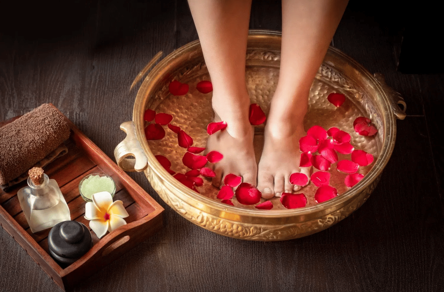A foot soak with rose petals in a copper bowl, with aromatherapy oils and stones nearby.