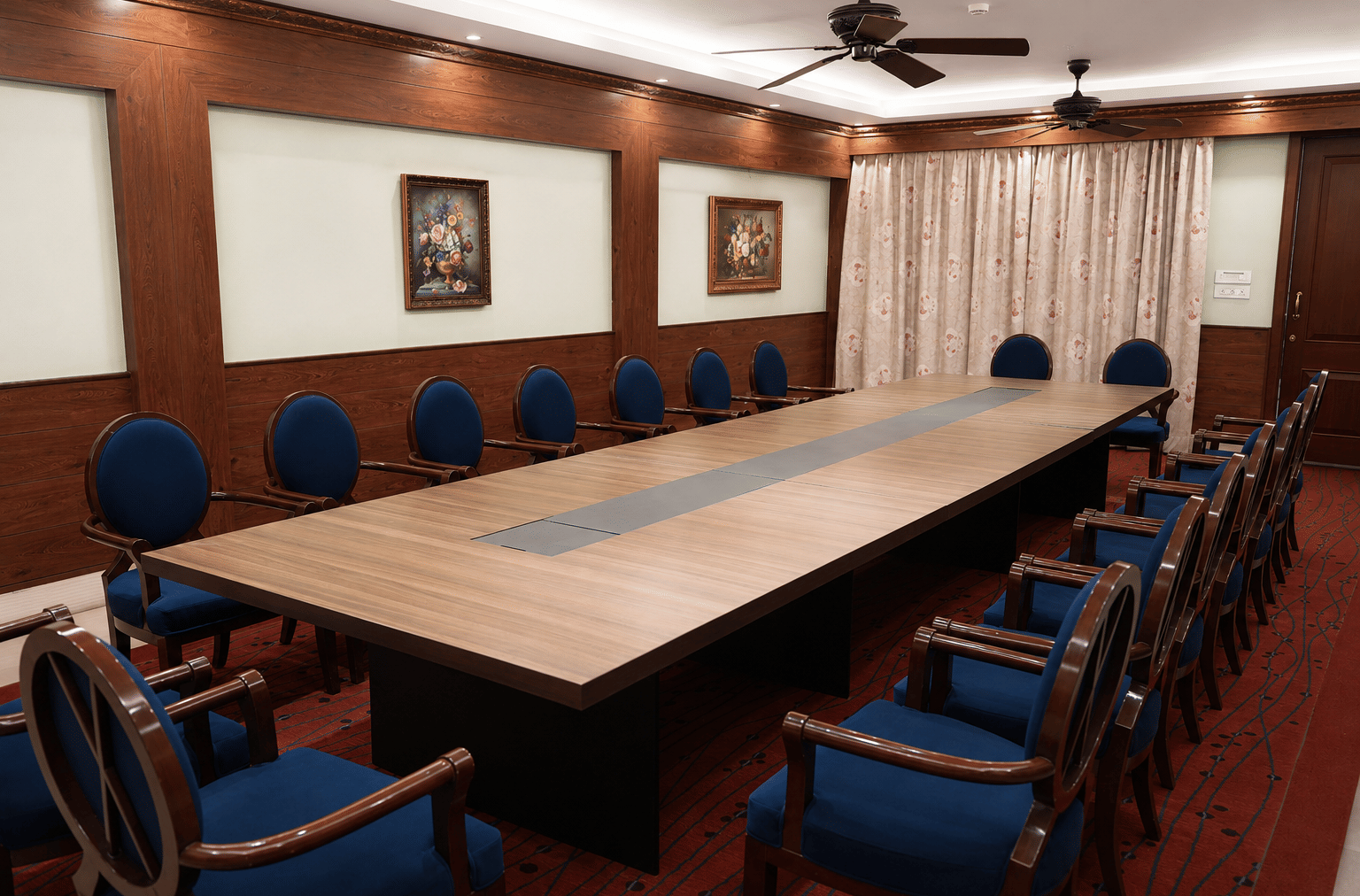 Camellia board room with a long wooden conference table, blue high-back chairs, panelled walls and floral paintings at MAYFAIR Himalayan Spa Resort, Kalimpong.
