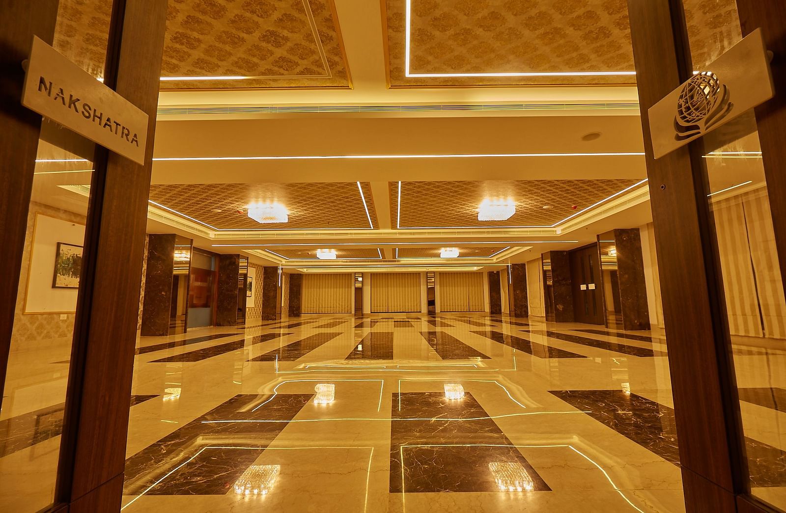 A long perspective of an empty, well-lit banquet hall with glossy, patterned floor tiles and decorative ceiling details.