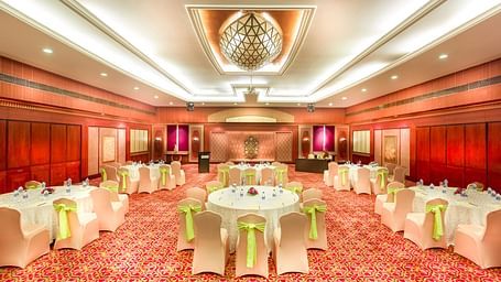 A wedding hall with white chairs tied with yellow ribbons pointing towards the stage at Grand Chennai By GRT Hotels.