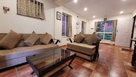 The spacious living area at Forest Escape offers comfortable seating, wooden furniture, and plenty of natural light, ideal for a family stay in Koyna.