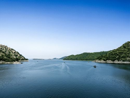 Expansive Jaisamand Lake, Alwar, under a clear blue sky with a few boats on the water