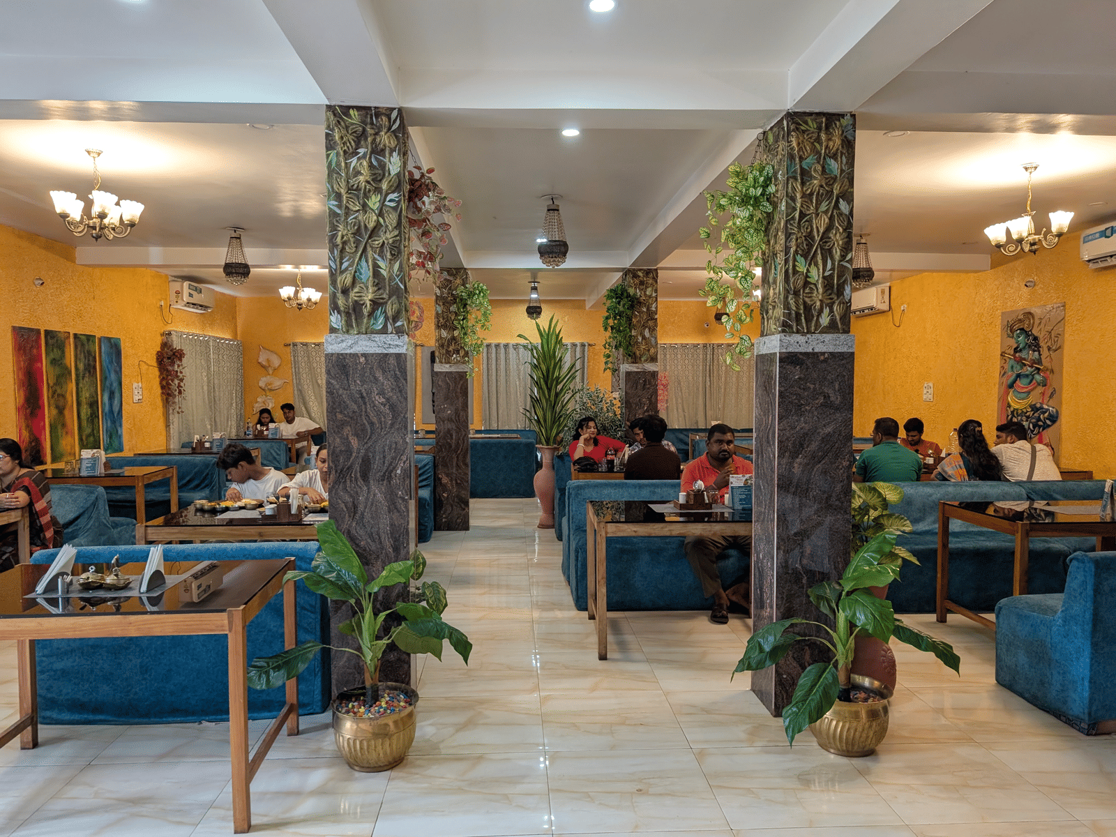Mache Vate Bengali restaurant's interior with sofa seatings, indoor plants, and warm lights at Dip Holidays.