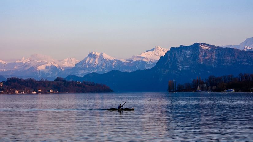 a boat in middle of a lake with snow covered mountains in the backdrop