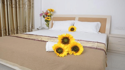 Deluxe Room at Biznotel by Pride, Bharuch featuring a double bed with sunflower bouquet on the bed runner and another bouquet in vase on the nightstand next to it