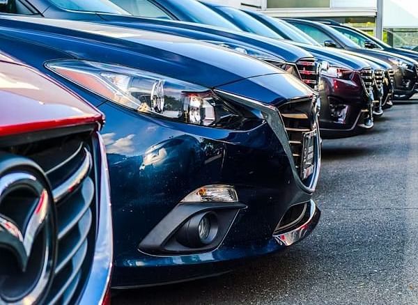 A close-up shows a row of parked cars, focusing on the front ends and headlights of the vehicles.