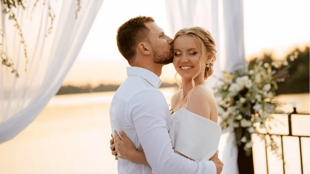 A couple in white attire shares a kiss against the backdrop of a sunlit beach, bathed in the warm glow of sunset - S Hotel Montego Bay, Jamaica