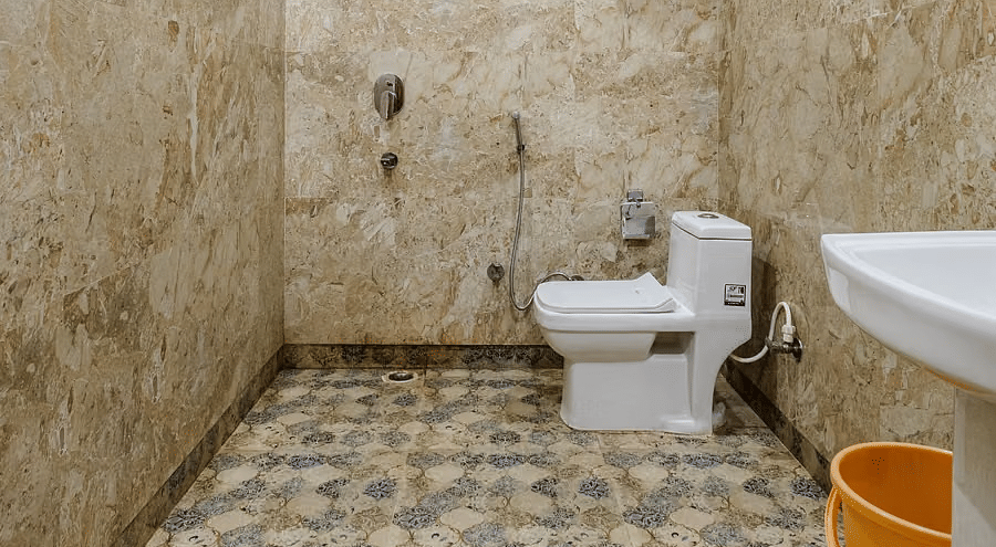 A spacious bathroom with one toilet and a washbasin, set against beige marble tiles - Lime Tree Hotels & Banquet, Vrindavan
