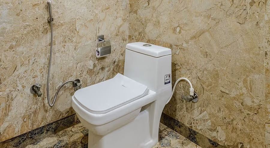 A bathroom with a toilet and jet spray fittings, featuring beige tiled walls - Lime Tree Hotels & Banquet, Vrindavan 