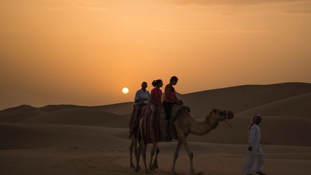 image of three people enjoying a camel back ride with a beautiful sunset in the background with sand dunes .