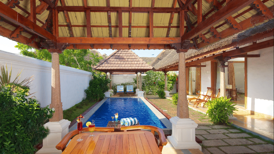 An outdoor private swimming pool area viewed from under a wooden gazebo structure | Le Pondy