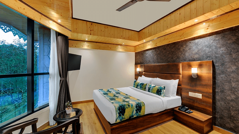 Premium Room  bedroom with a large bed and fan and a large window with outdoor views with chairs for seating - Sumi Queensyard, Darjeeling