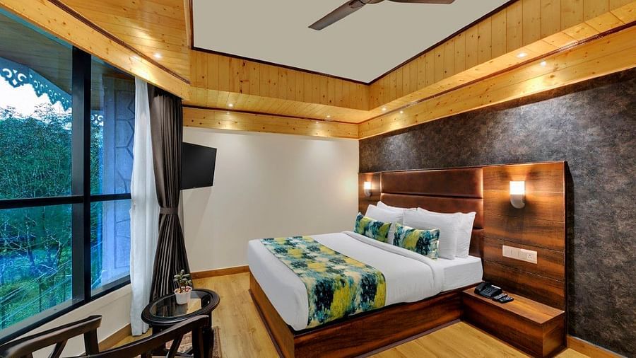 Premium Room  bedroom with a large bed and fan and a large window with outdoor views with chairs for seating - Sumi Queensyard, Darjeeling