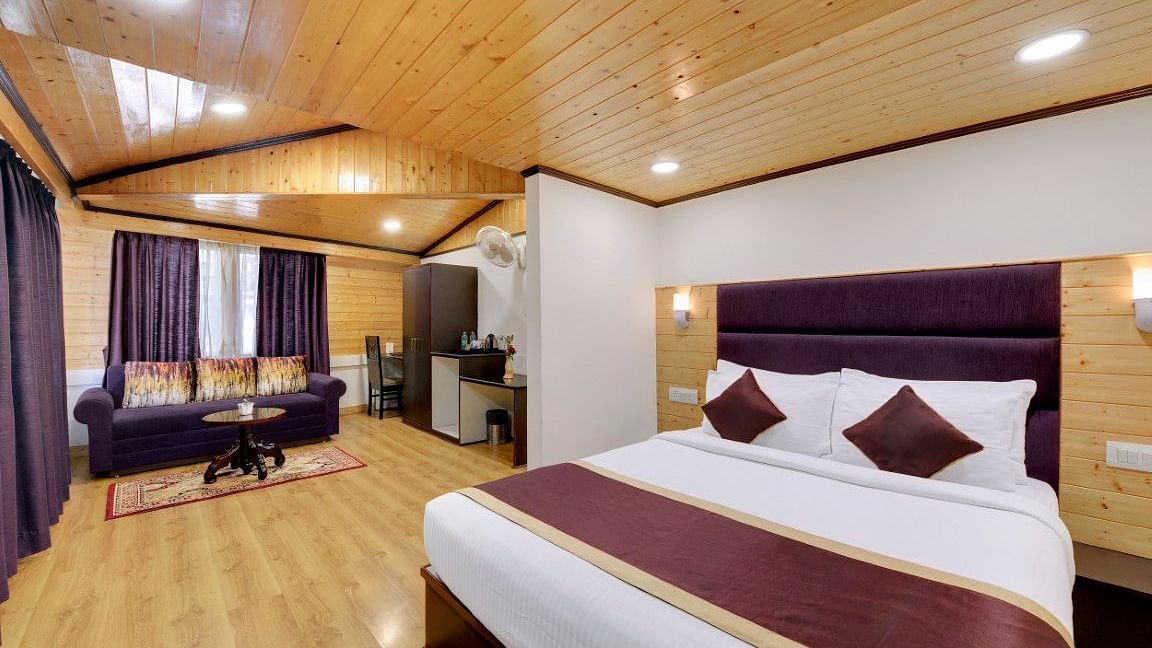 An image of a room with queen size bed leading to a living area with sofa, table and other amenities - Sumitel Darjeeling