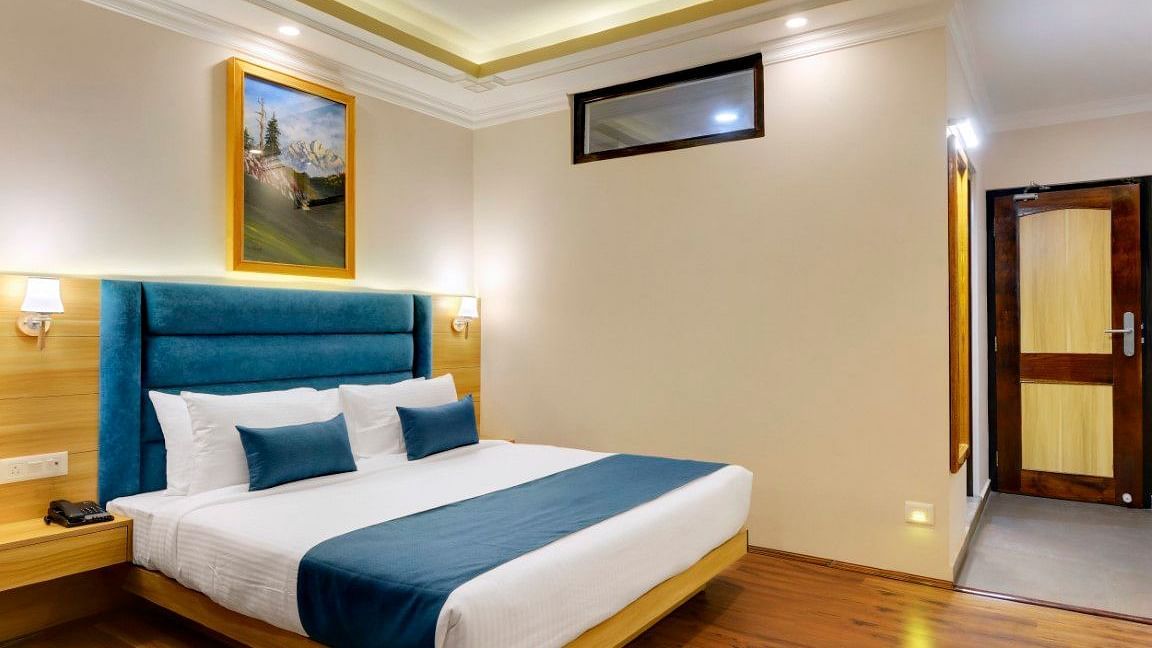 An image of a deluxe room with a bed, bed side table, lamps, and paintings hung on the wall - Yashshree Sikkim Blossom, Gangtok