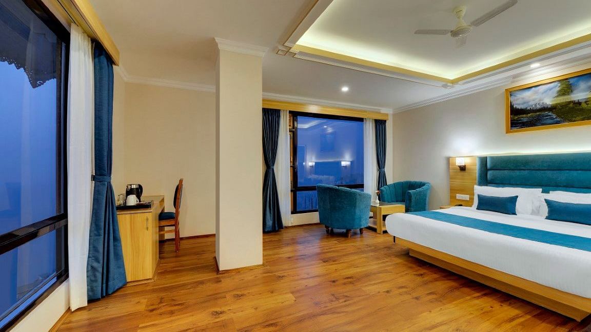 An image of the premium room with bed, sofa set, table, work, chair and an expansive window - Yashshree Sikkim Blossom, Gangtok