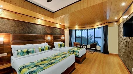 An image of Sumitel Queensyard premium room with king size bed and a single bed, tv, ceiling fan, and a chair and a table