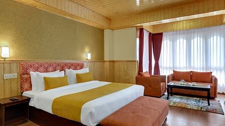 Image of a king size bed in an beautifully decorated room with wooden furnishing,a couch by the window  | Yashshree Lachung