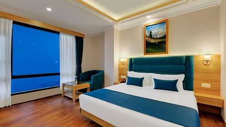 An image of the premium room with bed, bed side table, sofa, table and window overlooking the view - Yashshree Sikkim Blossom, Gangtok
