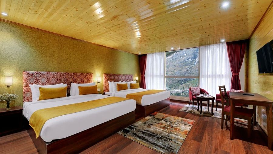 Image of two king size bed in an expansive room featuring wooden furnishing an a window overlooking the mountains  | Yashshree Lachung