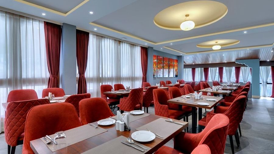 Shot of  the restaurant at the hotel with red chair and tables with plates arranged  | Yashshree Lachung