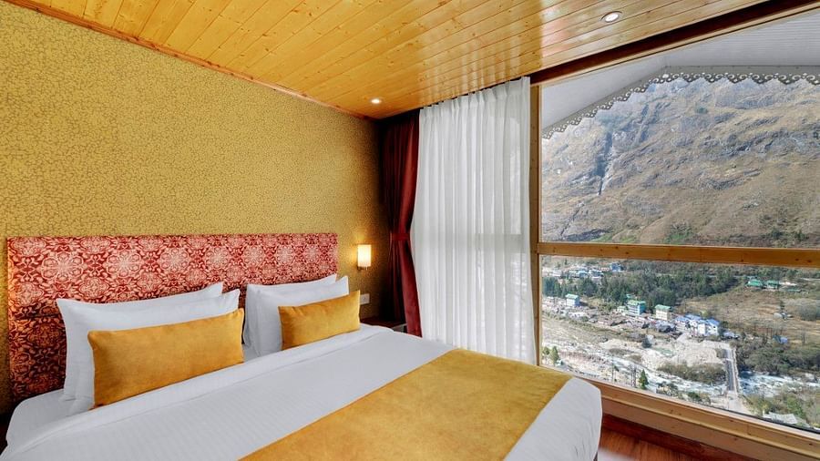 Image of a room at our hotel with wooden ceiling and flooring featuring a bed beside an expansive window overlooking the mountains  | Yashshree Lachung