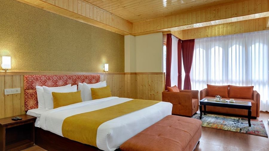 Shot of a premium room at our hotel featuring a kind size bed, a couch and a cosy seating space with an expansive window that overlooks the mountains | Yashshree Lachung