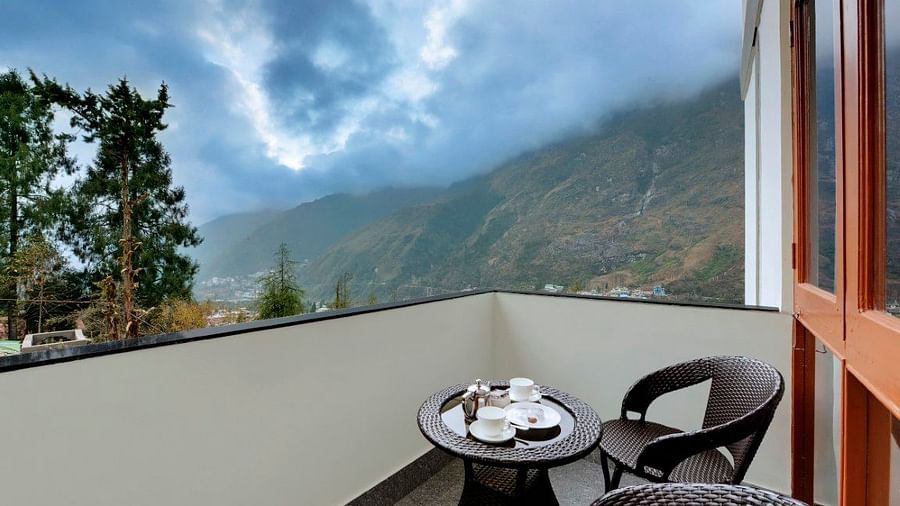 View of the lush green mountains from the balcony of a room at our resort featuring two chairs and a small table  | Yashshree Lachung